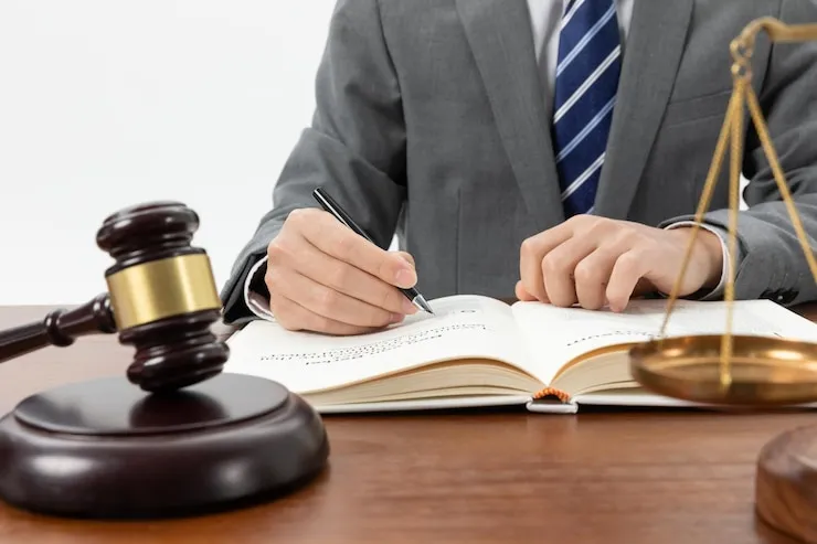 An attorney signing a legal document beside a gavel and the scales of justice, representing wills, trusts, and estate planning documents prepared by Osman Law